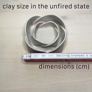 May include: A nested, unfired clay bowl set. The set includes two bowls, one inside the other, with a heart-shaped design. The text "clay size in the unfired state" and "dimensions (cm)" are visible. A ruler is placed next to the bowls.