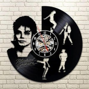 Puede incluir: Reloj de vinilo negro con la silueta de Michael Jackson y bailarines. La esfera del reloj es visible, con un diseño mecánico detallado. Las palabras "Michael Jackson" están escritas en el disco.