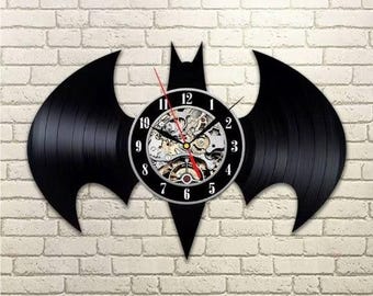 Könnte beinhalten: Schwarze Batman-förmige Wanduhr. Die Uhr besteht aus einer wiederverwendeten Schallplatte. Das Zifferblatt ist schwarz mit weißen Ziffern und sichtbaren Zahnrädern. Der Sekundenzeiger ist rot. Die Uhr ist an einer weißen Backsteinmauer befestigt.