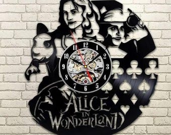 Könnte beinhalten: Schwarze Alice im Wunderland Wanduhr. Die Uhr zeigt ein schwarzes Silhouettendesign von Charakteren aus der Geschichte, darunter Alice, der Hutmacher und Spielkartenfarben. Das Zifferblatt hat einen sichtbaren Getriebemechanismus.