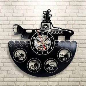 May include: Black vinyl record clock cut into the shape of a submarine. The clock face is visible, with a skeleton design. The submarine has portholes with silhouettes of people waving. The clock is mounted on a white brick wall.