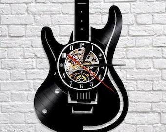 Könnte beinhalten: Schwarze Gitarren-Wanduhr mit weißem Zifferblatt und rotem Sekundenzeiger. Das Zifferblatt der Uhr zeigt sichtbare Zahnräder und ein klassisches analoges Design. Die Uhr ist an einer weißen Ziegelmauer befestigt.