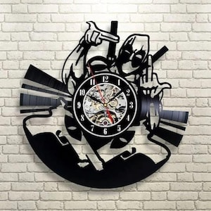 May include: Black vinyl record clock featuring a Deadpool design. The clock has a black and white face with visible gears and red hands. The design includes the character's silhouette and iconic gestures, mounted on a brick wall.