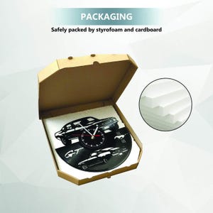 K&ouml;nnte beinhalten: Eine schwarze Wanduhr mit Auto-Motiv und rotem Sekundenzeiger, verpackt in einem Karton mit Styroporpolsterung. Die Uhr zeigt Autosilhouetten und den Text "GT". Die Verpackung ist mit "PACKAGING" beschriftet.