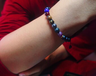 May include: A beaded bracelet featuring a variety of colorful beads, including blue, red, brown, and black. The bracelet is worn on a wrist and has a black string closure. The beads have different textures and patterns.