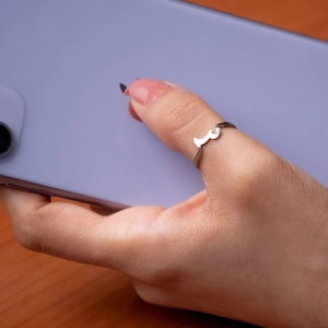 May include: A silver ring with a stylized Arabic letter on a person's finger.