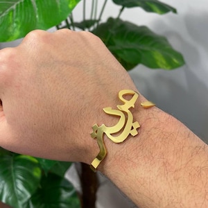 May include: A gold-colored bracelet with a name written in Arabic script.