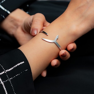 May include: A silver bracelet with a Y-shaped design. The bracelet is open and adjustable.