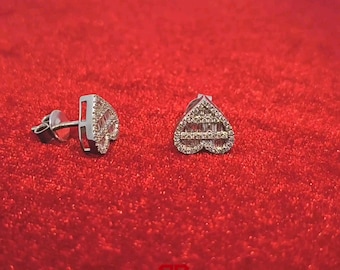 May include: A pair of silver heart-shaped earrings with small diamonds set in a pave setting. The earrings are on a red background.