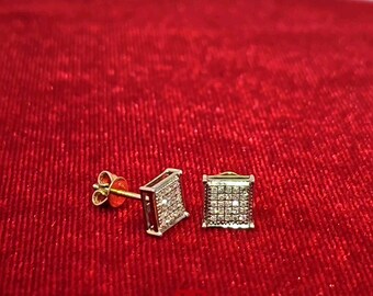 以下が含まれることがあります： 金色の枠にセットされた正方形のダイヤモンドのイヤリングのペア。イヤリングは赤いベルベットの背景の上に置かれています