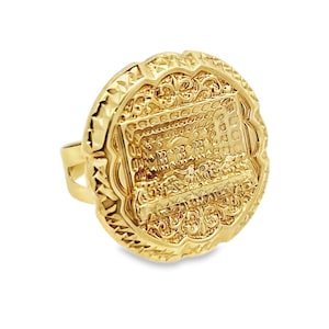 Può includere: Un anello d'oro con un grande volto rotondo ornato. Il volto dell'anello presenta un design dettagliato di una scena con figure e motivi intricati.