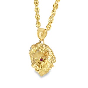 May include: A gold-colored lion pendant necklace. The pendant features a detailed lion's head with a red gem eye. The chain is a thick, twisted rope style. The jewelry is displayed against a white background.