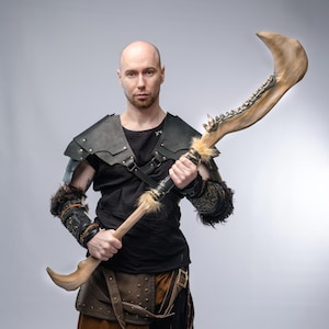 May include: A large, curved weapon with a bone-like blade and wooden handle. The weapon features decorative elements and is held by a person wearing black leather armor and fur accents. The overall aesthetic suggests a fantasy or cosplay theme.