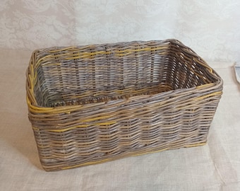 May include: Rectangular woven basket in shades of gray, brown, and yellow. The basket is made of woven wicker and has a sturdy, open design. The basket is ideal for storage or display.