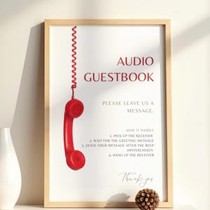 以下が含まれることがあります： 「AUDIO GUESTBOOK」の文字とメッセージの残し方の説明が書かれた額縁入りのサイン。赤い電話の受話器が上から吊り下げられています。装飾的な松ぼっくりが下にあります。