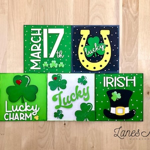 May include: Four wooden signs with a St. Patrick's Day theme. The signs feature shamrocks, a horseshoe, a leprechaun hat, and the text "March 17th", "Lucky", "Lucky Charm", and "Irish".