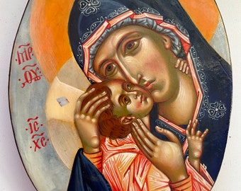 Könnte beinhalten: Eine handgemalte Ikone, die die Jungfrau Maria zeigt, die das Jesuskind hält. Die Ikone ist in traditionellem Stil mit goldenen Akzenten und blauem Hintergrund gemalt. Der Text "IC XC" ist in der linken unteren Ecke sichtbar.