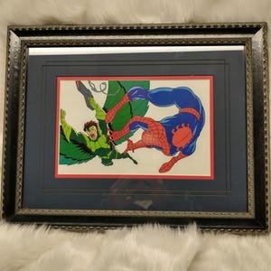May include: A framed illustration of Spider-Man fighting the Green Goblin. The image is set against a white background and features a red, white, and blue border. Spider-Man is in mid-air, kicking the Green Goblin, who is wearing a green suit and a mask.