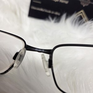 Puede incluir: Gafas rectangulares negras con lentes transparentes. La montura tiene una barra de metal con la inscripci&oacute;n "63-18" en el lateral.