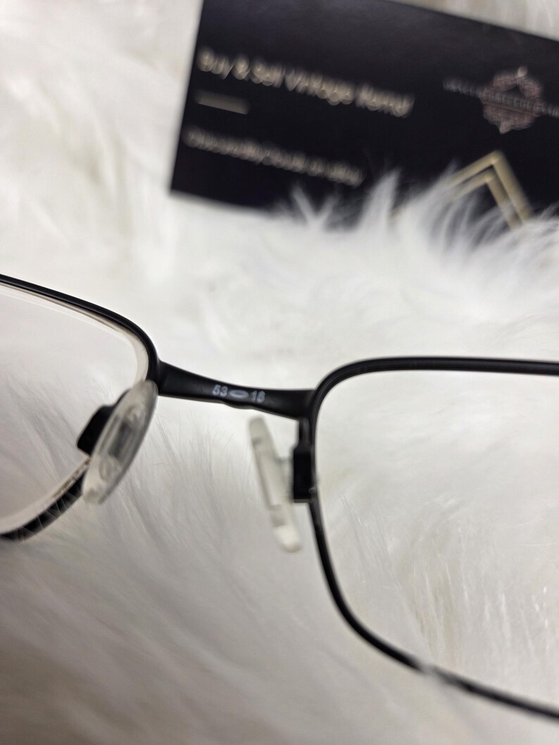 Puede incluir: Gafas rectangulares negras con lentes transparentes. La montura tiene una barra de metal con la inscripci&oacute;n "63-18" en el lateral.