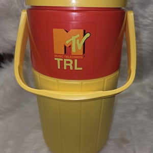 May include: A yellow and red MTV TRL branded beverage container. The container has a yellow lid and base, with a red center section featuring the MTV logo and TRL text. It includes a yellow handle.