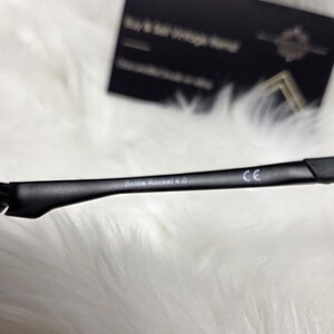 Puede incluir: Primer plano del marco negro de unas gafas de sol con el texto "Dolce Rocket 4.0" y "CE" impreso en el marco.