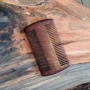 May include: A dark brown wooden comb with fine teeth. The comb has a rounded shape and is made of a smooth, polished wood.