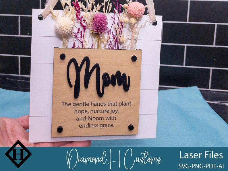 May include: A wooden sign with the word "Mom" in black lettering and a quote about the gentle hands that plant hope, nurture joy, and bloom with endless grace. The sign is decorated with dried flowers.
