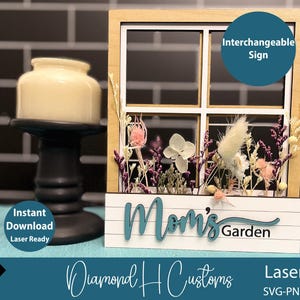 May include: A wooden window frame with a white background and a sign that says "Mom's Garden". The window frame is decorated with dried flowers and greenery. The sign is interchangeable.