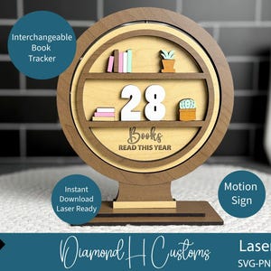 May include: A wooden book tracker with a circular design. It features shelves with miniature books and a plant, displaying the number "28" and the text "Books READ THIS YEAR". The base is rectangular.