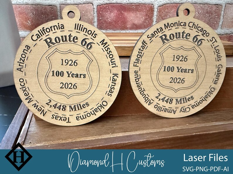 May include: Two wooden Route 66 commemorative ornaments. Each ornament is circular with engraved text including "Route 66", "1926", "100 Years", "2026", and "2,448 Miles". The ornaments are made of light-colored wood.
