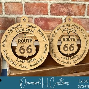 May include: Two wooden Route 66 ornaments. Each ornament features a circular design with the route's name and the number 66 in the center. The outer ring includes the names of cities and states along the route, and the distance of 2,448 miles.