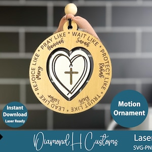 May include: A wooden motion ornament with a heart-shaped cutout and a cross. The ornament has the words "Pray Like Hannah", "Wait Like Sarah", "Rejoice Like Mary", and other phrases. The text "Motion Ornament" is also visible.