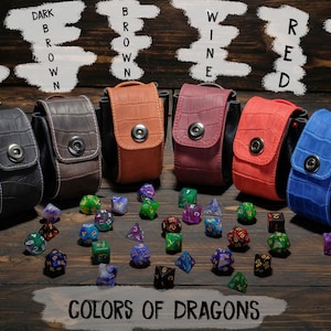 May include: Six different colored leather dice bags with a snap closure. The bags are arranged in a row on a wooden surface. The bags are labeled with the colors: black, dark brown, brown, wine, red, and blue. The bags are surrounded by colorful dice.