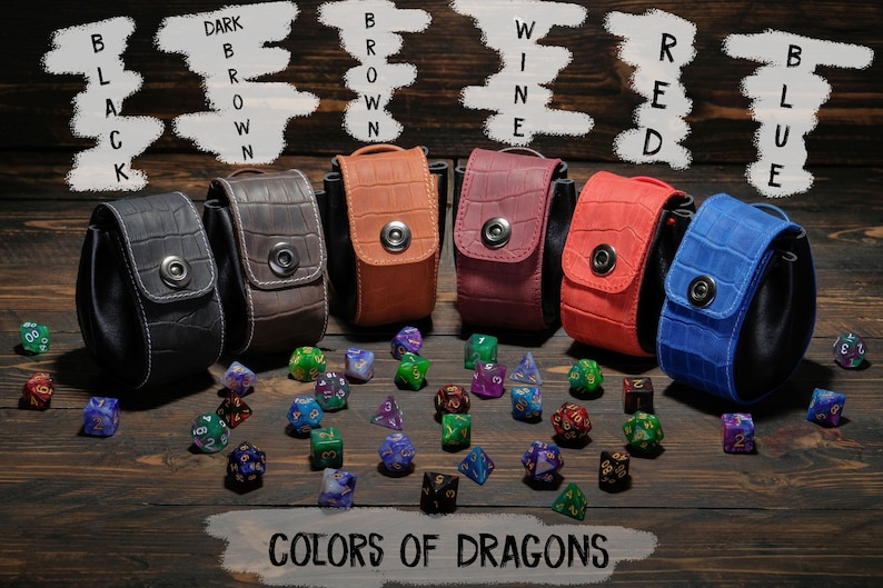 May include: Six different colored leather dice bags with a snap closure. The bags are arranged in a row on a wooden surface. The bags are labeled with the colors: black, dark brown, brown, wine, red, and blue. The bags are surrounded by colorful dice.