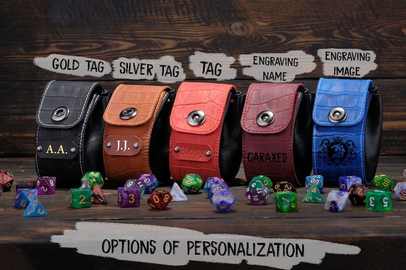 May include: Five different colored leather dice bags with various personalization options. The bags are lined up on a wooden surface with dice scattered in front of them. The options include a gold tag, silver tag, a tag, engraving a name, and engraving an image.