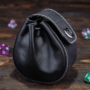 May include: Black leather dice bag with white stitching and a silver snap closure. The bag is filled with colorful dice.