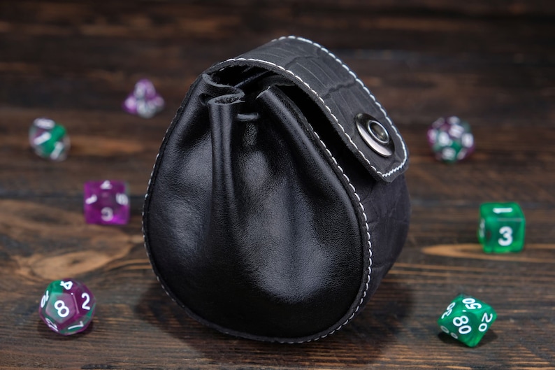 May include: Black leather dice bag with white stitching and a silver snap closure. The bag is filled with colorful dice.