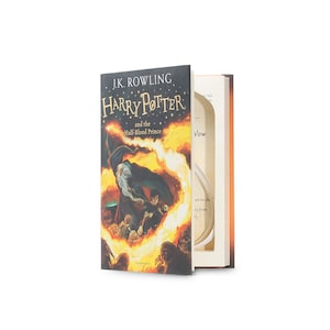 Peut inclure: Un livre fermé avec un compartiment caché. La couverture présente une illustration d'Harry Potter et Dumbledore sur un fond de feu. Le texte sur la couverture est "J.K. Rowling Harry Potter et le Prince de Sang-Mêlé".