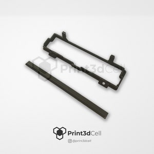 Può includere: Due pezzi di plastica nera, uno un telaio rettangolare e l'altro una striscia lunga e sottile. Il telaio ha un piccolo foro nell'angolo in basso a destra. La striscia ha una superficie testurizzata. Print3dCell è stampato nell'angolo in basso a destra dell'immagine.