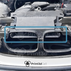 Könnte beinhalten: Nahaufnahme eines schwarzen Kunststoff-Motorlufteinlasses mit zwei rechteckigen Öffnungen. Der Lufteinlass ist Teil eines Automotorraums.
