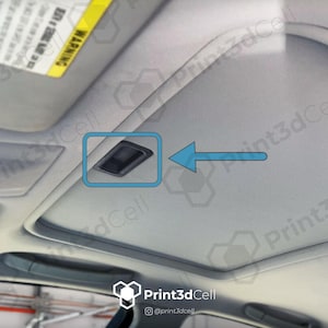 Puede incluir: Primer plano del techo interior de un coche, con una lámpara de techo rectangular negra. La imagen está tomada desde un ángulo bajo, con una flecha azul que apunta a la luz. El interior del coche es gris claro.