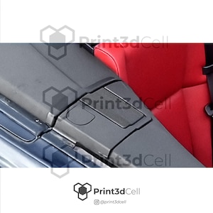 Op de afbeelding: Detailopname van een auto-interieur, met een grijze console en een klein, rechthoekig compartiment. De achtergrond toont een rode stoel en een zwarte veiligheidsgordel. Het Print3dCell-logo is zichtbaar.