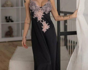 Puede incluir: Un camisón negro largo hasta el suelo con delicados detalles de encaje rosa claro a lo largo del escote en V profundo y el dobladillo. La prenda tiene tirantes finos y una silueta suave y fluida que llega hasta los tobillos.