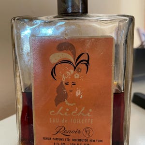 May include: Vintage perfume bottle of "Chichi Eau de Toilette" by Renoir. The rectangular glass bottle has a dark brown cap and a peach-colored label with a woman's silhouette. The bottle contains 8 fl. oz. of perfume.