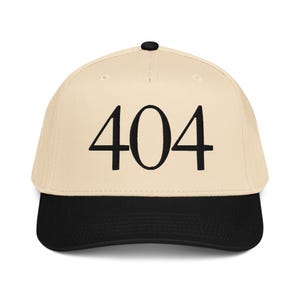 May include: A baseball cap with a cream-colored crown and a black brim. The number "404" is embroidered in black on the front of the cap. The cap has a black button on top.
