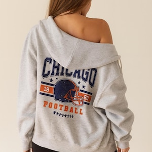 May include: A gray hoodie with the word "CHICAGO" in navy blue arched across the top, with a football helmet graphic in the center. The hoodie also features the words "FOOTBALL" and the numbers "19" and "20".