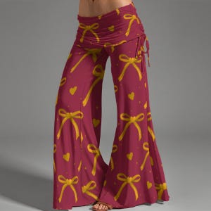 May include: Burgundy palazzo pants with a repeating pattern of yellow bows and hearts. The pants have a wide leg and a ruched waistband with drawstring detail. The fabric appears to be soft and flowing, suitable for casual wear.