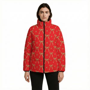 May include: A red puffer jacket with a repeating pattern of gold bows and small gold hearts. The jacket has a black zipper and a high collar. The model is wearing black pants.