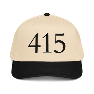 May include: A baseball cap with a cream-colored crown and a black brim. The number "415" is prominently displayed in black on the front of the cap. The cap has a curved bill and a black button on top.